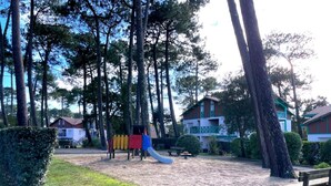 A playground with a slide and climbing structures, surrounded by trees and a few buildings in the background. - T2 Apartment mezzanine with terrace and pets allowed (Soustons)