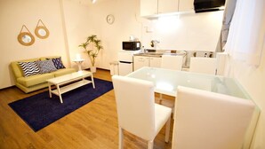 Espaço compacto com sofá, mesa de centro, mesa de jantar, cadeiras, micro-ondas e pequena cozinha.