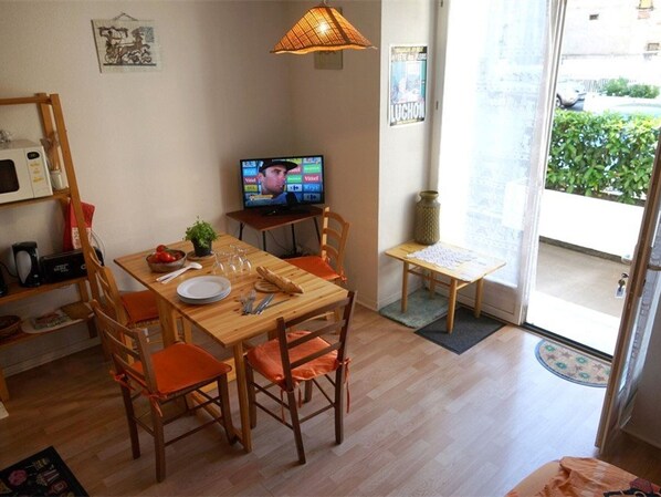 Un comedor con una mesa de madera, sillas naranja, un televisor y un ventanal con vistas a zonas verdes.