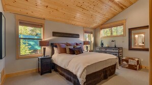 A bedroom with a wooden ceiling, a bed with multiple pillows, a nightstand, a dresser, and a mirror.
