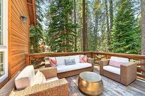 A wooden deck with wicker furniture and a round table, surrounded by tall trees.