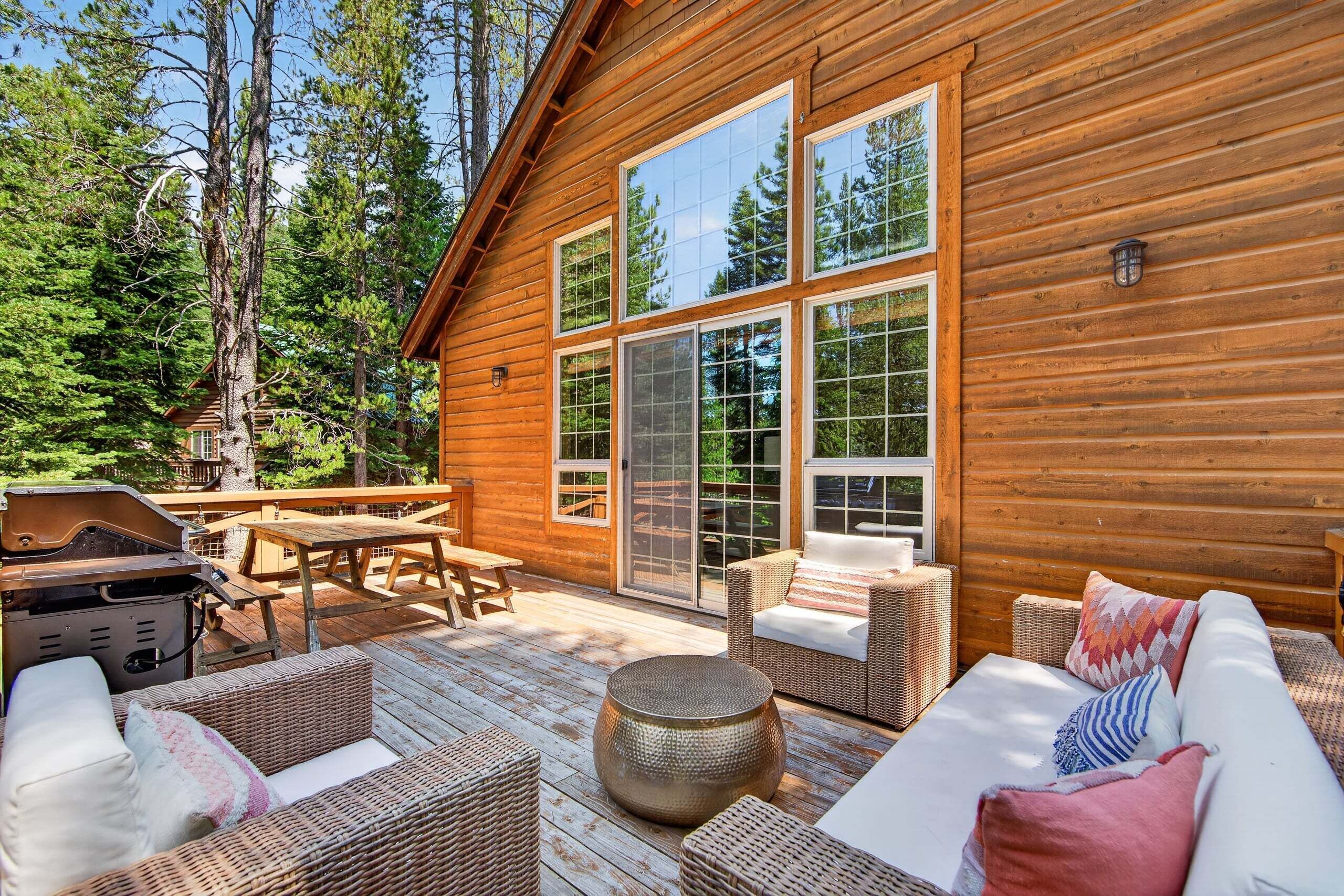 A wooden cabin with a deck, wicker furniture, and a barbecue grill.