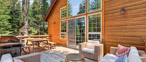 A wooden cabin with a deck, wicker furniture, and a barbecue grill.