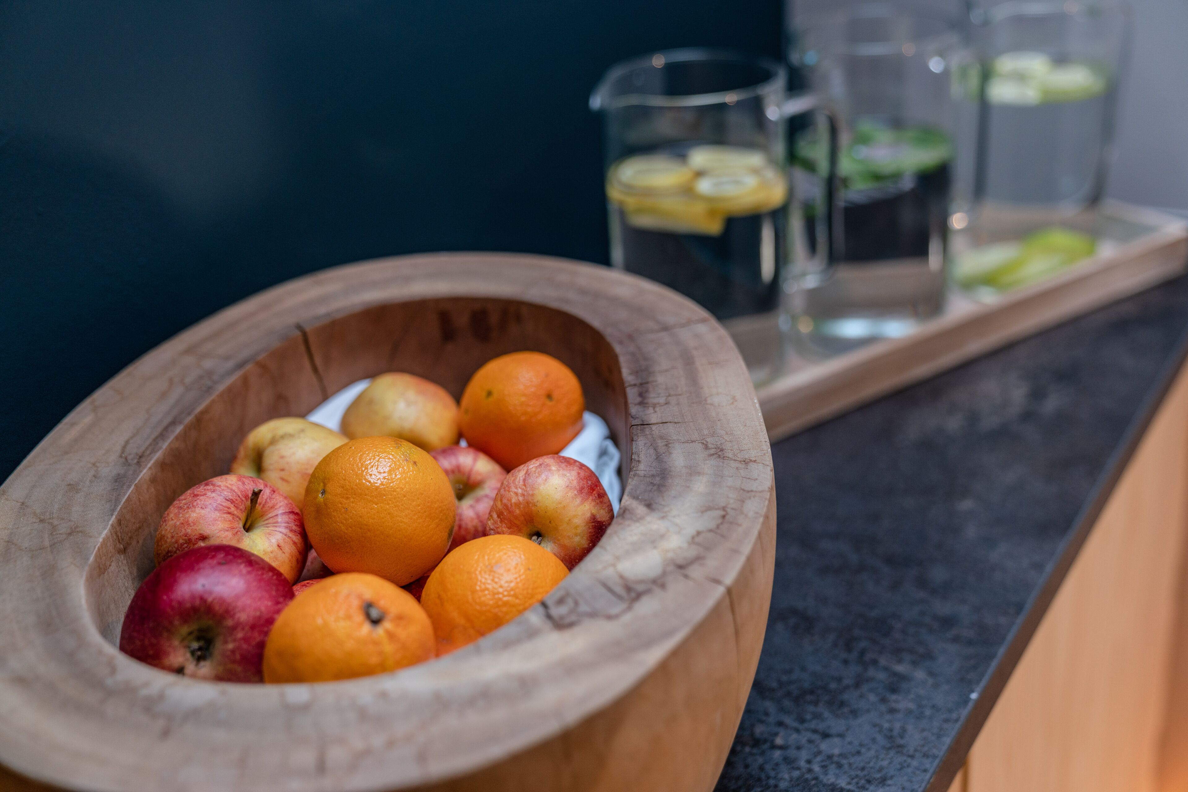 A wooden bowl filled with apples and oranges on a kitchen counter.