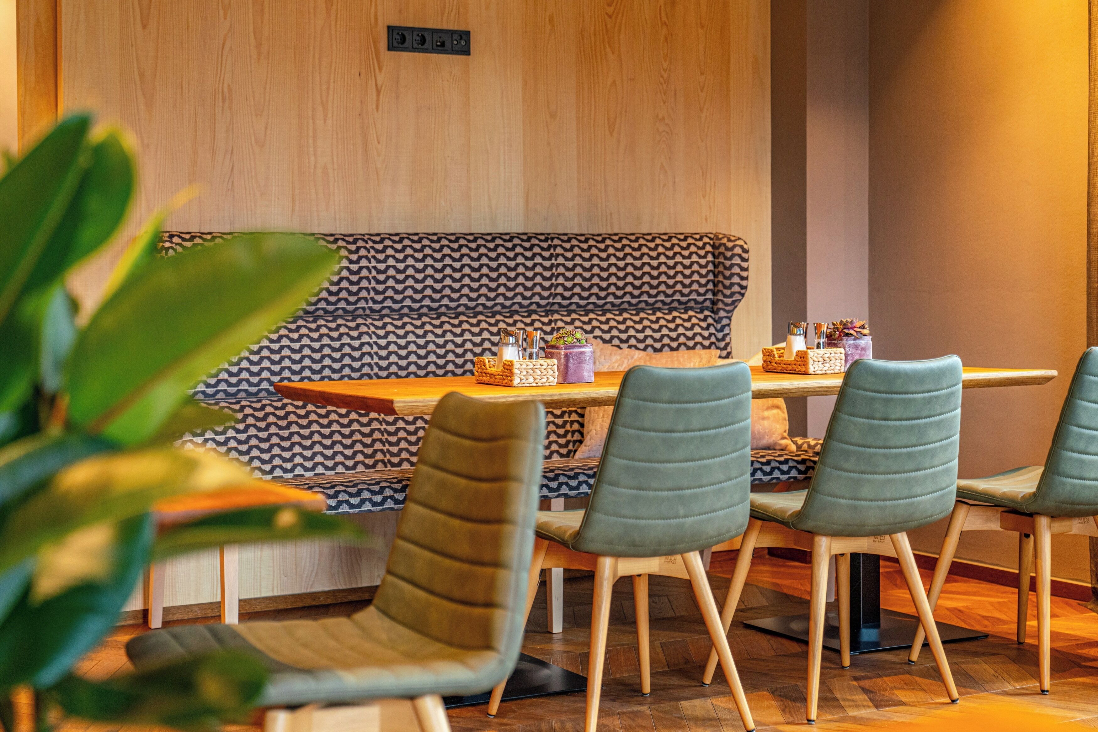 Een moderne eetruimte met een houten wand, een gestreept bankje en groene bekleden stoelen.