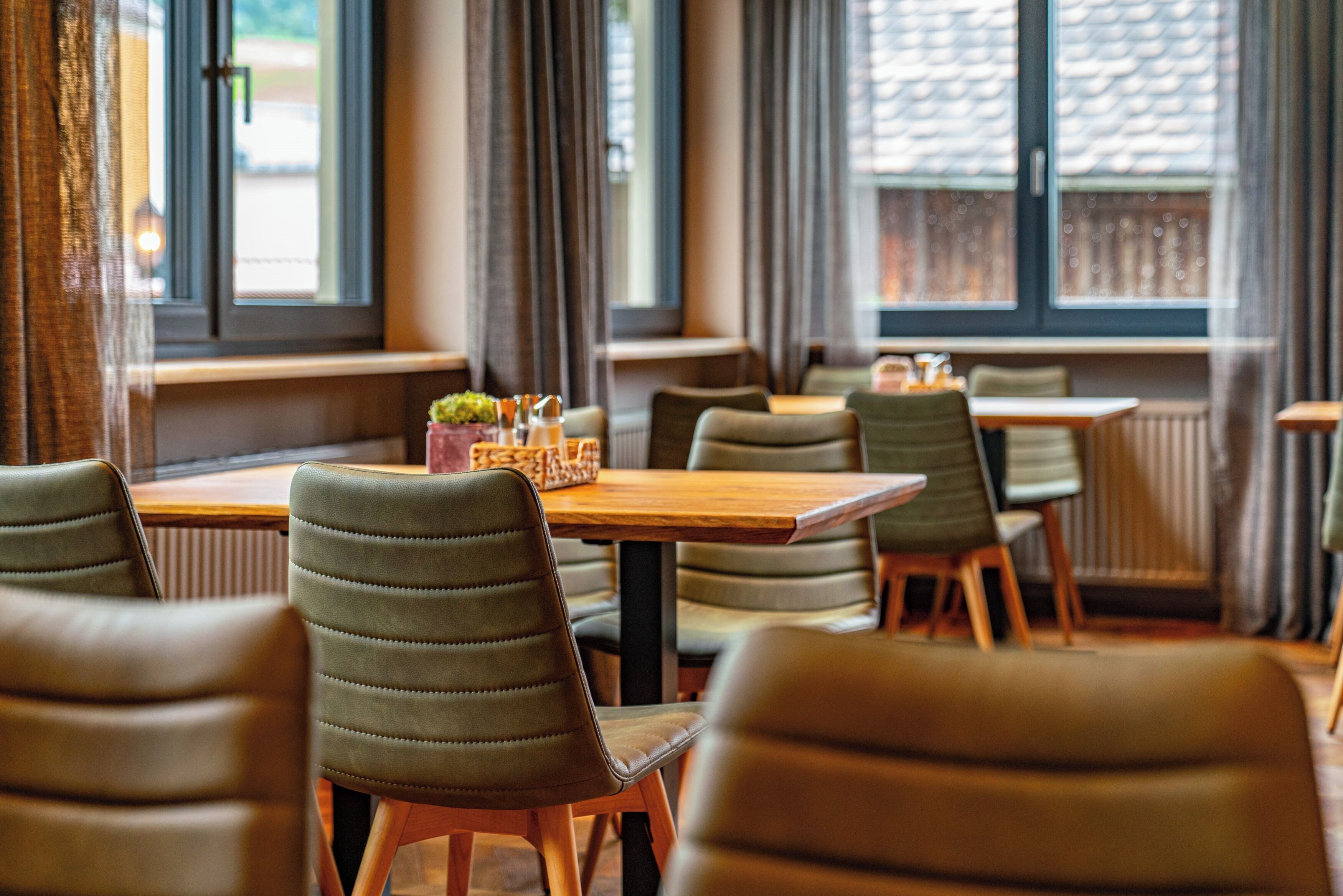A dining area with wooden tables and green upholstered chairs.