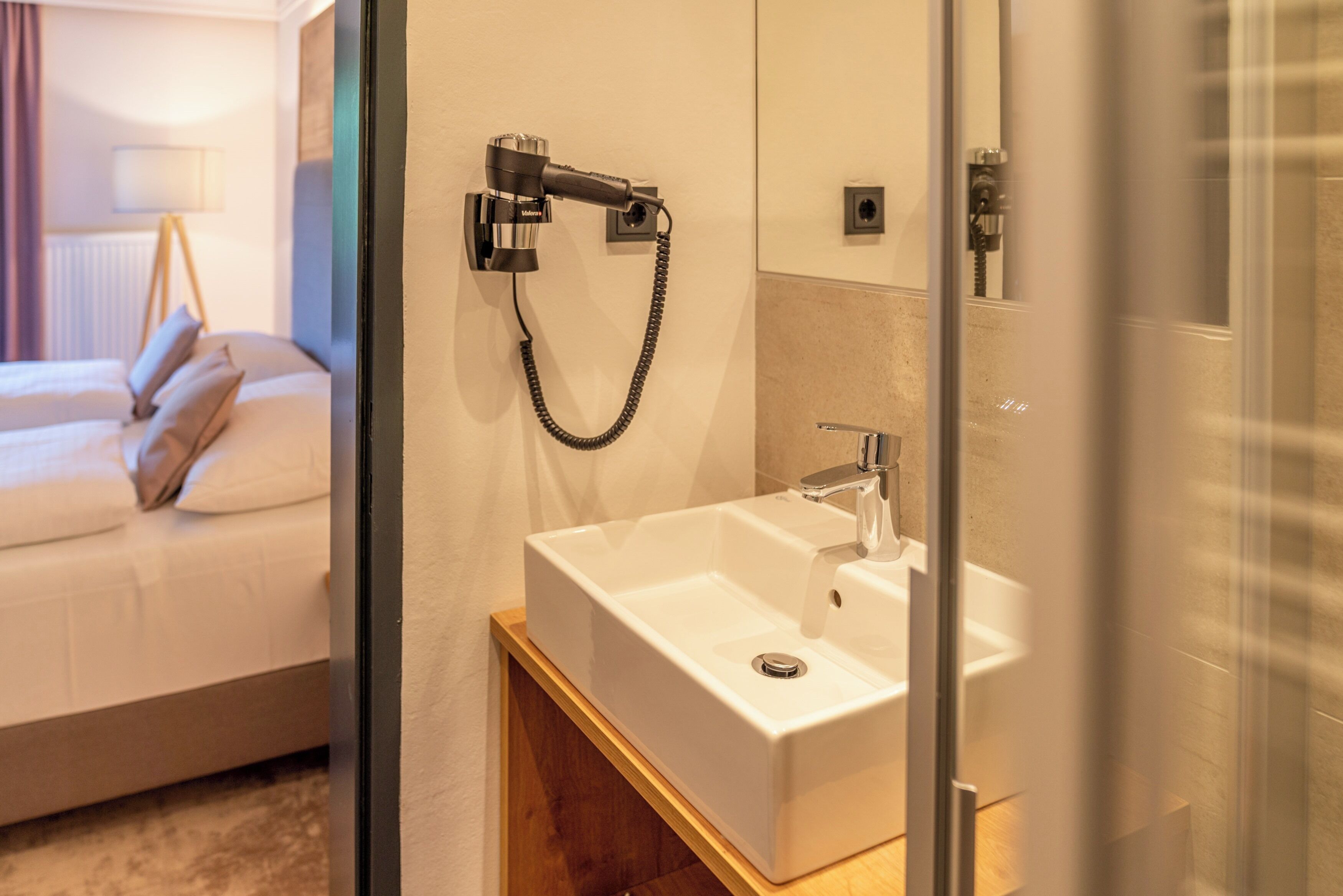 A hotel bathroom with a white sink, a handheld showerhead, and a mirror.