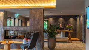 A modern lobby with a wooden ceiling, a large potted plant, a seating area with a chair, and a reception desk. - Stadtvilla Schladming Boutiquehotel (Schladming)