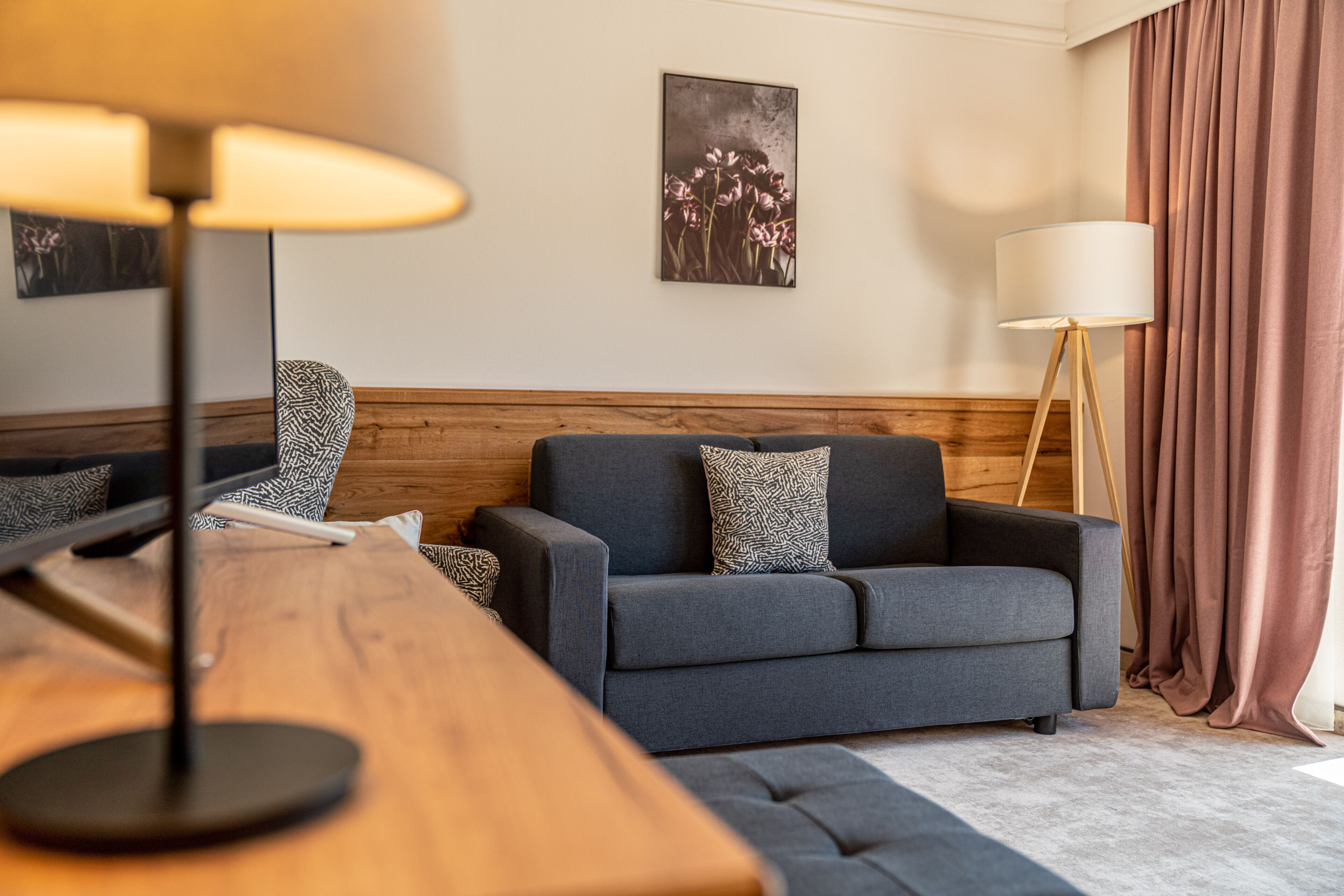 Ein modernes Wohnzimmer mit grauem Sofa, einem Holzsideboard und einer Stehlampe.