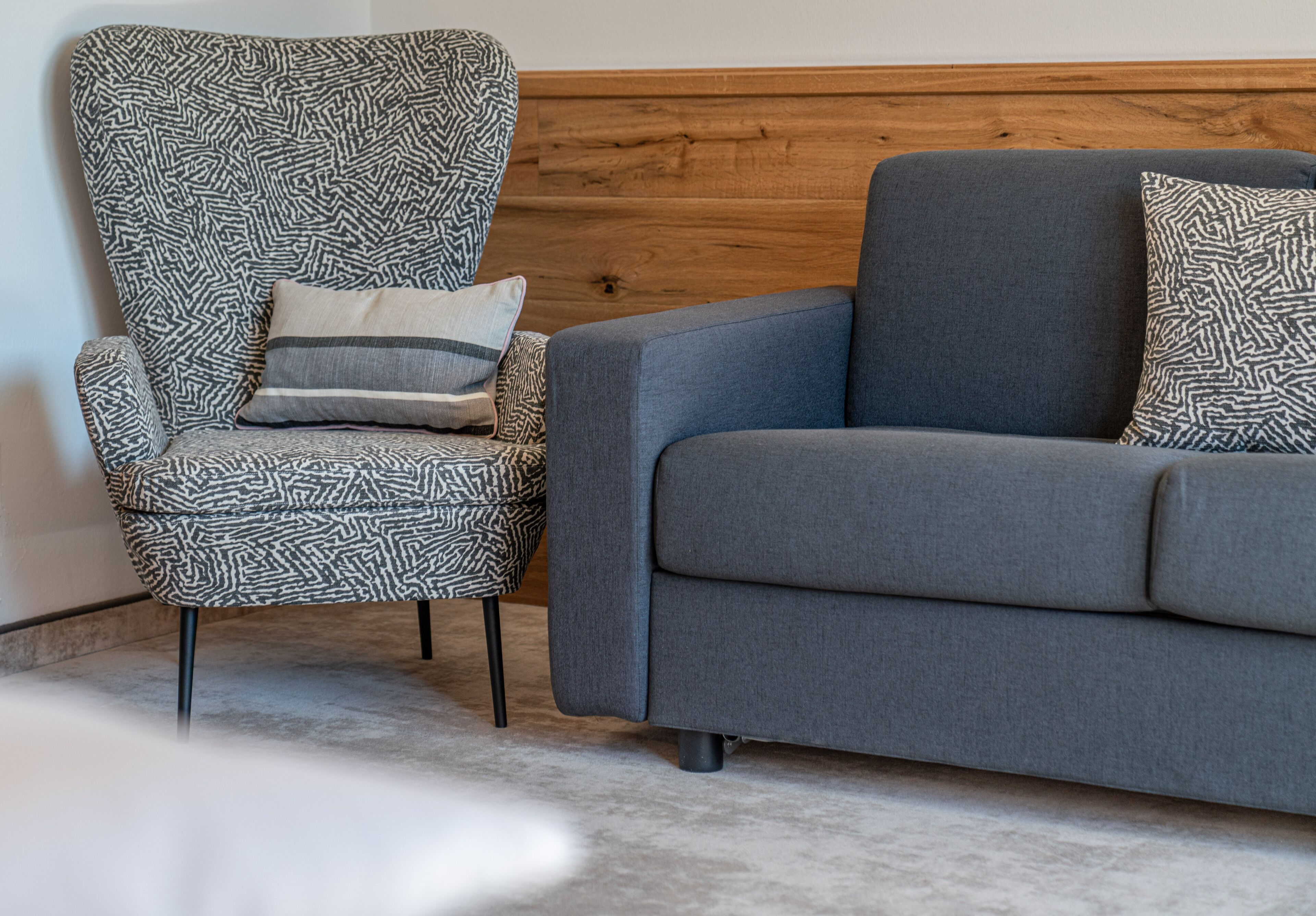 Una sala moderna con un sillón estampado, un sofá gris y cojines a juego.