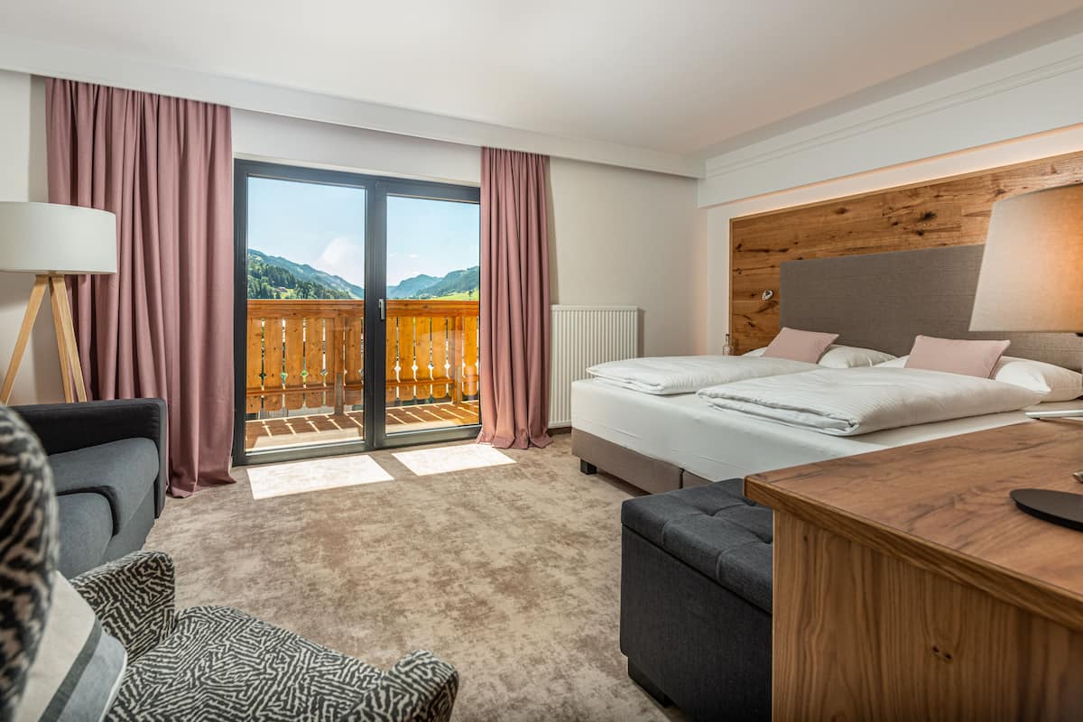 A hotel room with a bed, a desk, a chair, a lamp, and a view of the mountains through the balcony doors.