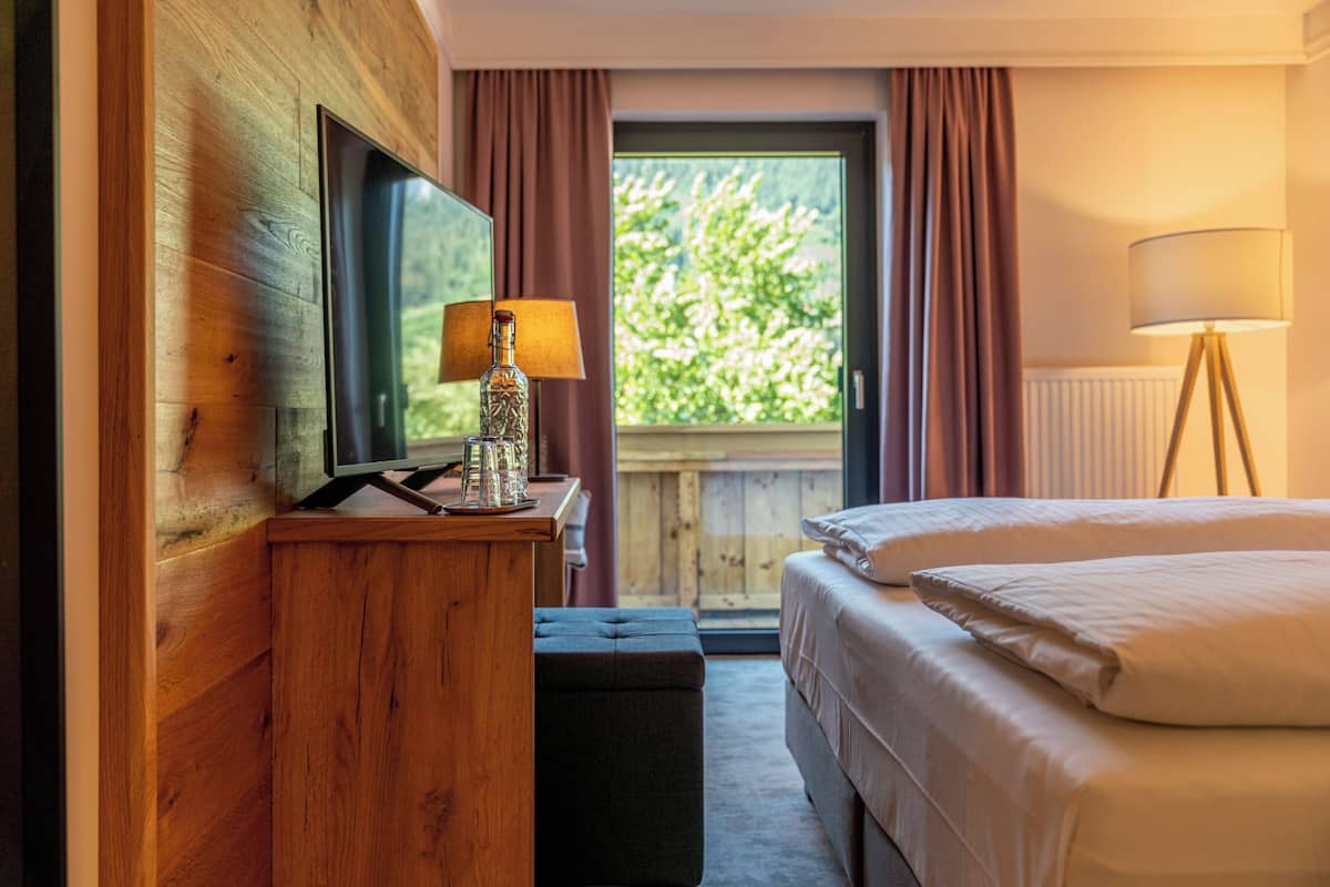A hotel room with a wooden desk, a television, a lamp, a bed, and a window with curtains.