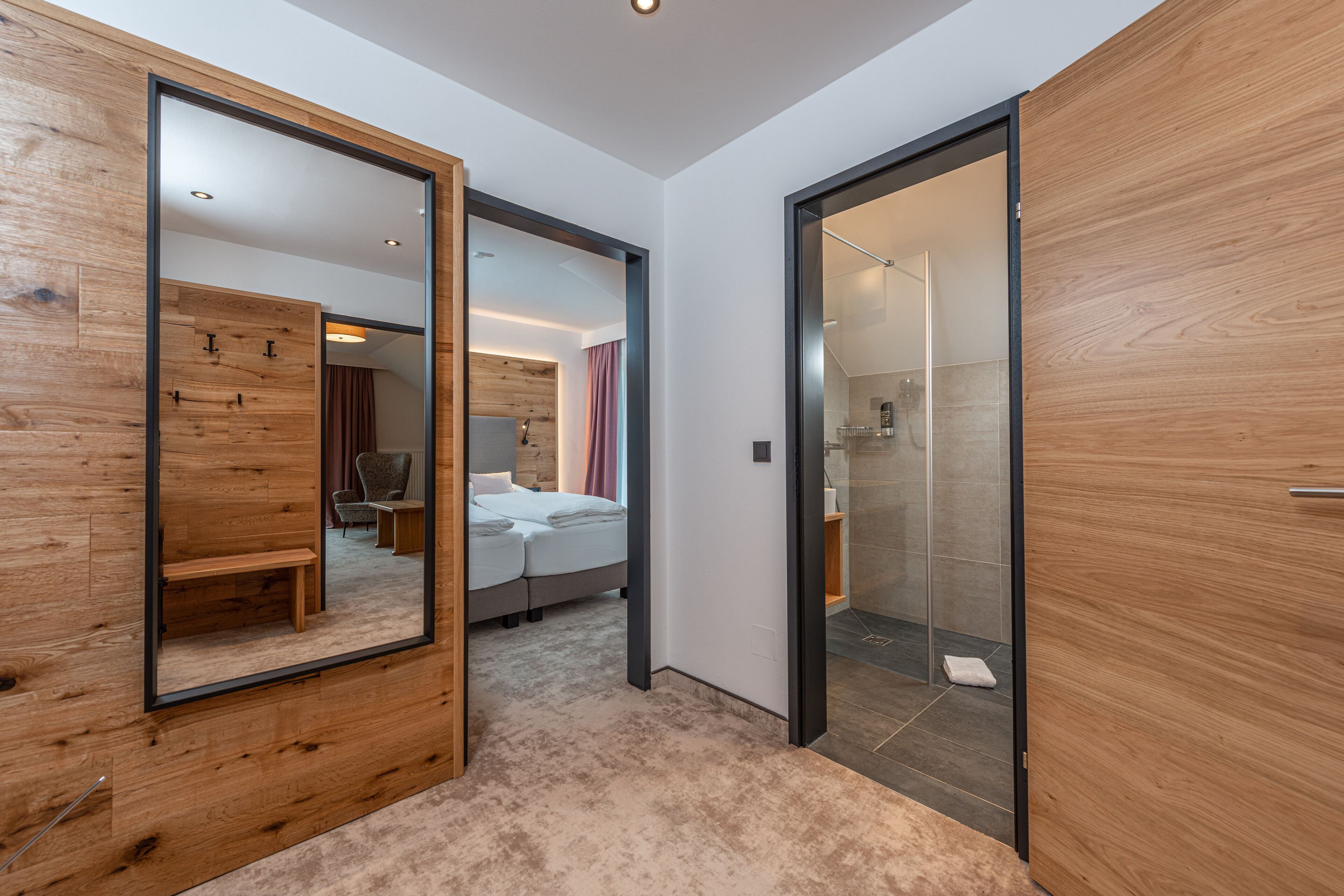 Una habitación de hotel moderna con un espejo grande, una cama, un banco y una zona de ducha.