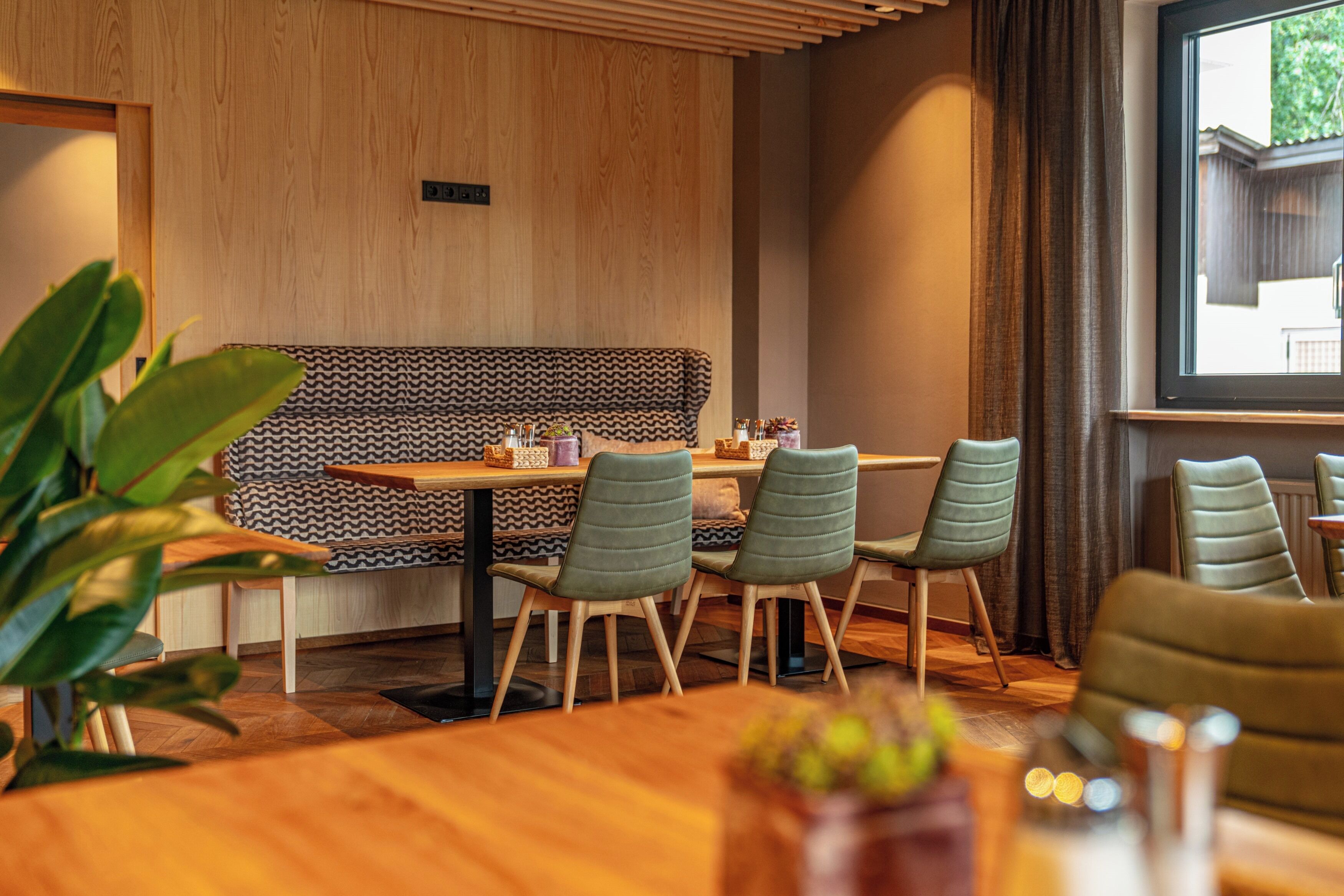 A restaurant interior with wooden panel walls, a patterned bench, and green upholstered chairs.