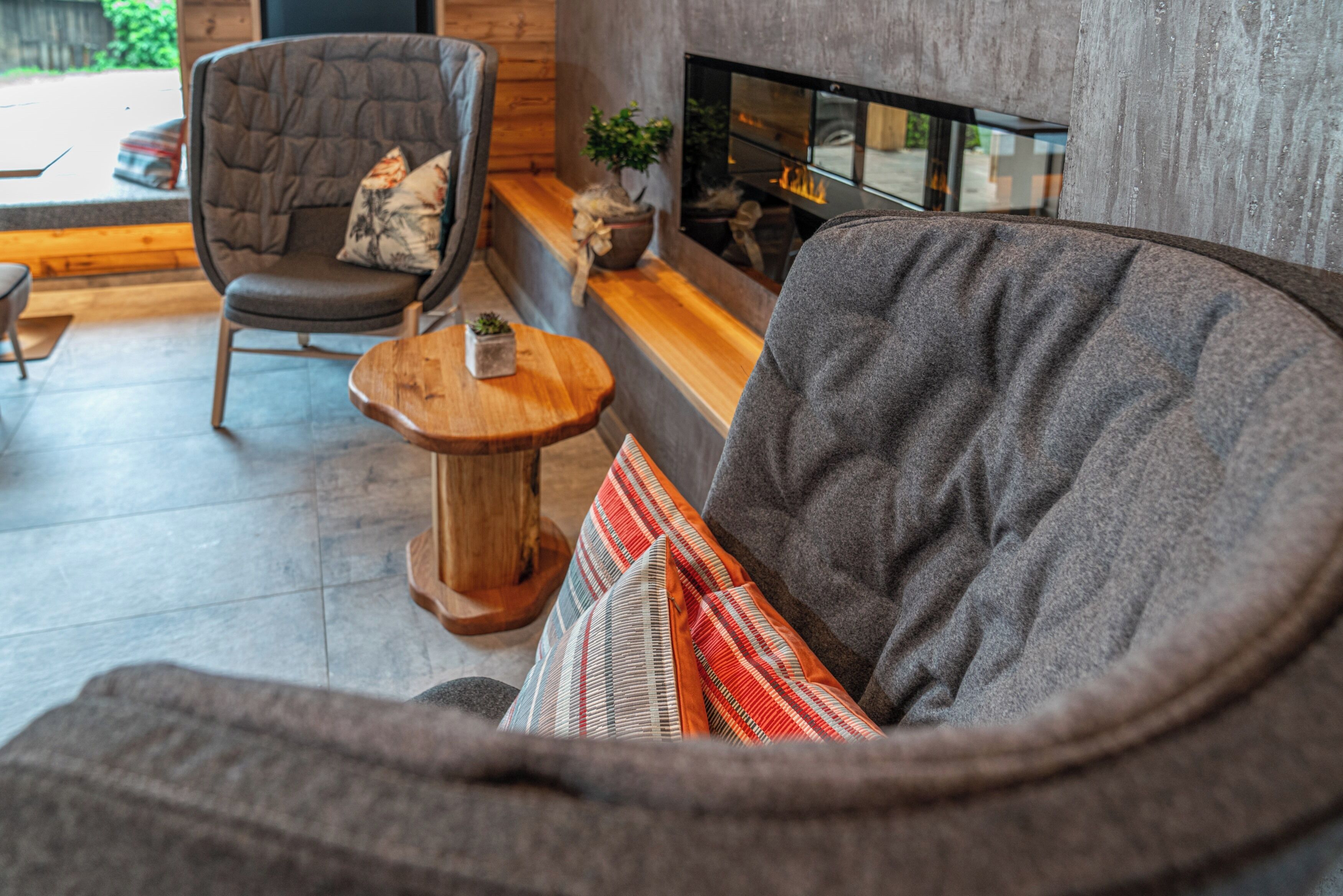 Een gezellige zithoek met een grijze bank, een houten bijzettafeltje en een fauteuil met een kussen.