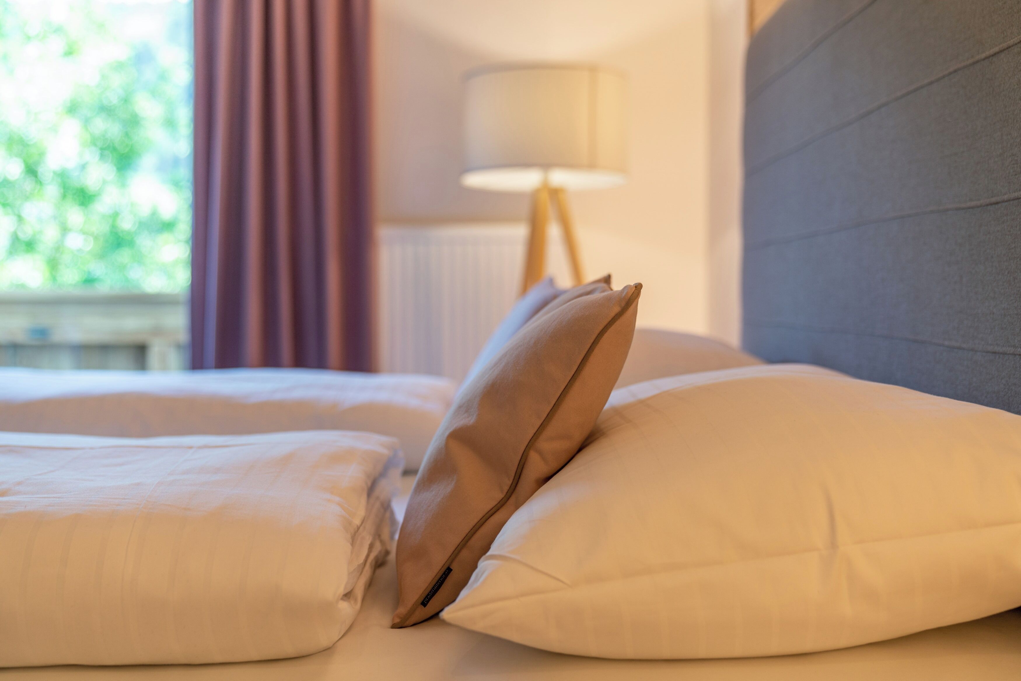 A neatly made bed with white linens and two beige pillows.