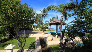 Ein tropisches Resort mit Pool, Liegestühlen und einem Gazebo mit Reetdach.