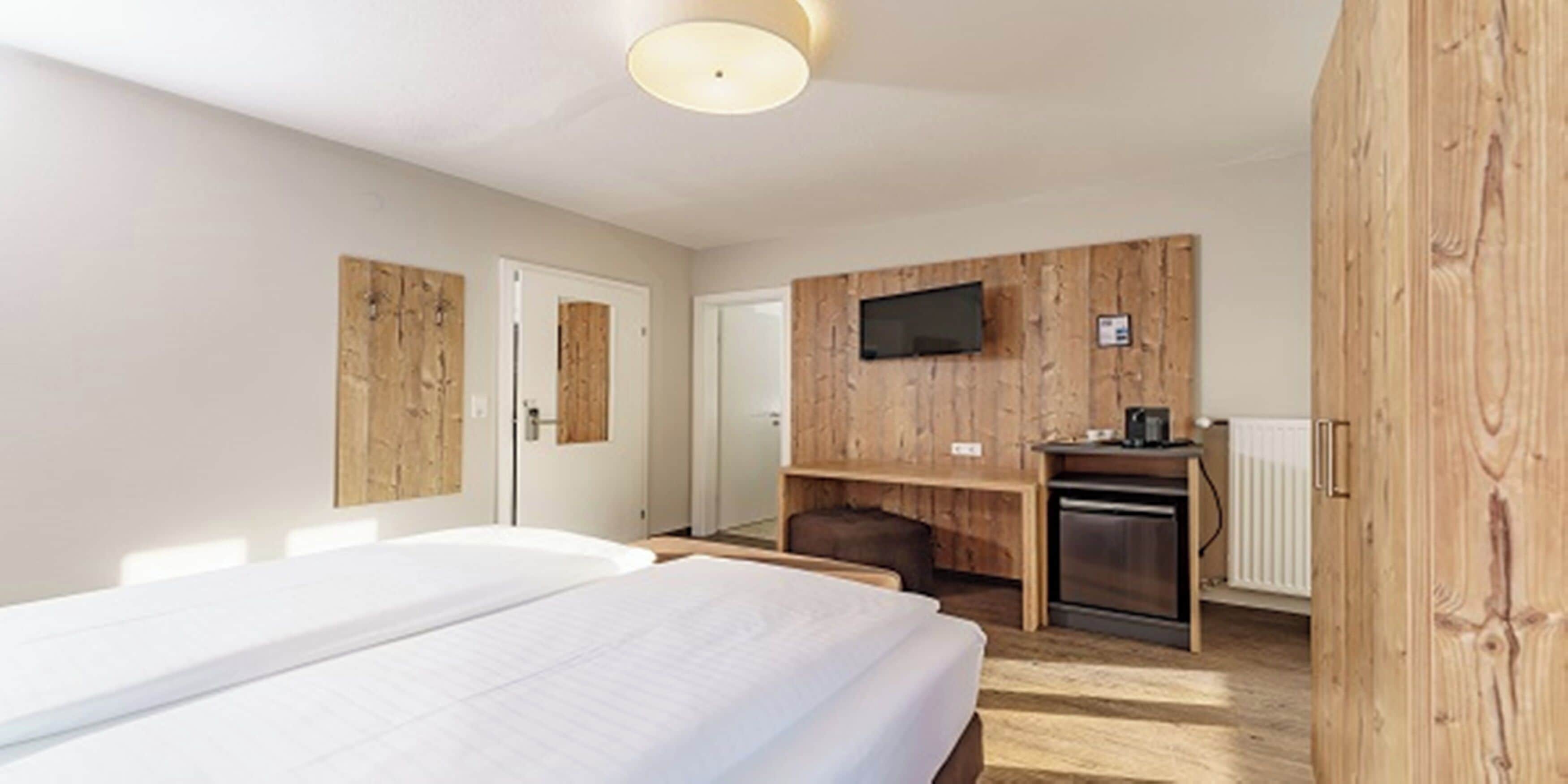 A modern hotel room with a large bed, a wooden accent wall, a TV, and a kitchenette.