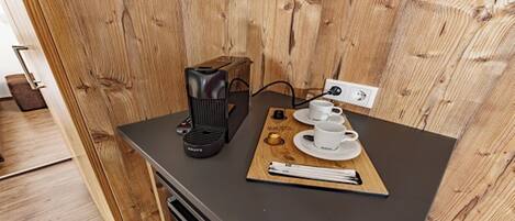 A wooden wall with a black coffee maker and two white cups on a tray.
