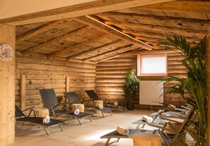 Une cabane en rondins, avec des murs et un plafond en bois, aménagée avec plusieurs chaises longues et une plante en pot.