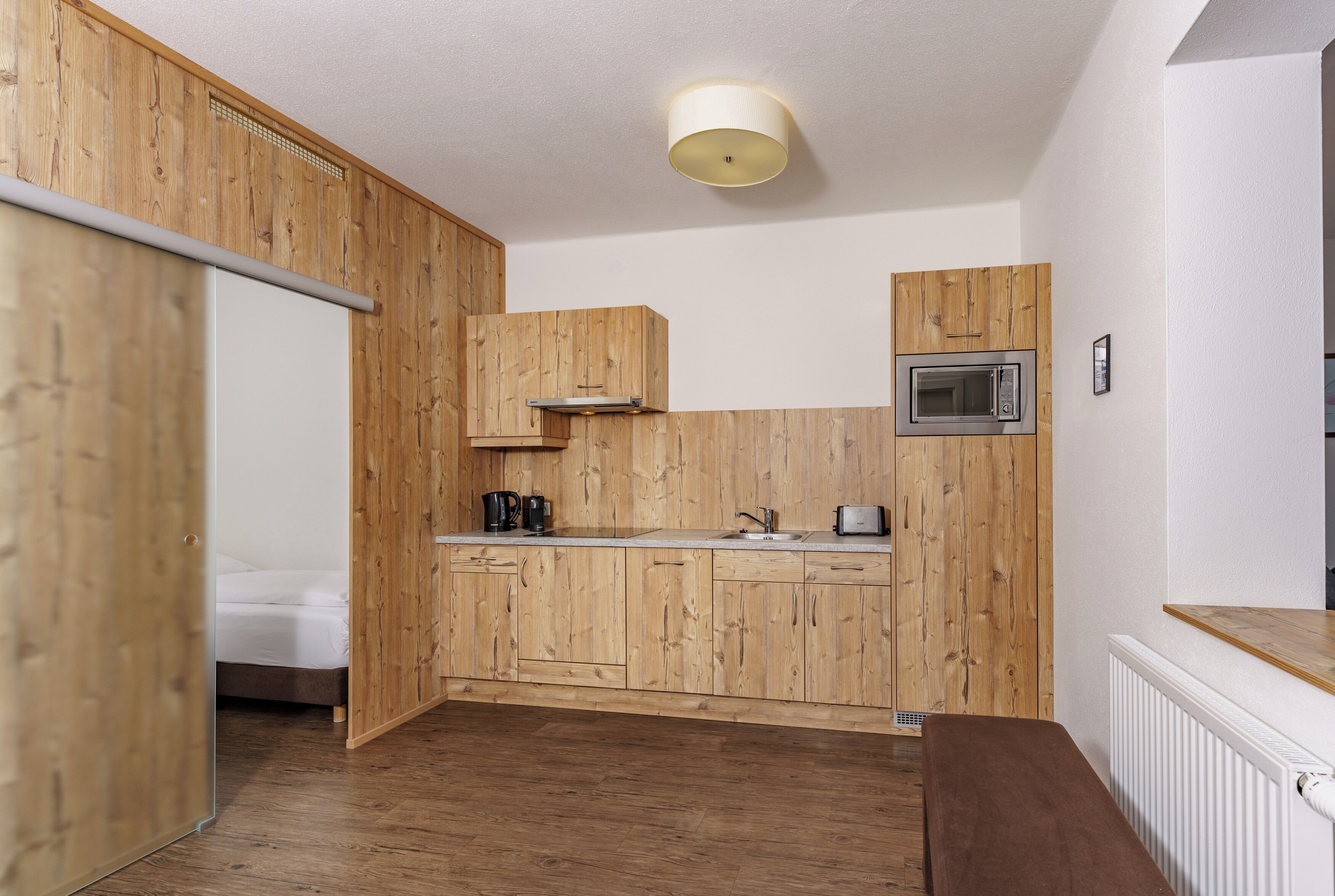 Cocina compacta con armarios de madera, microondas, lavamanos y encimera.