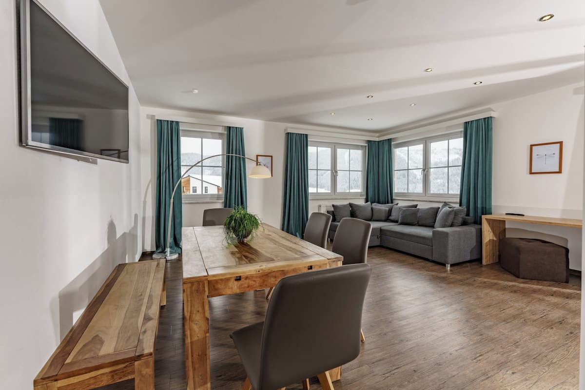 Un salon moderne avec une table à manger en bois, un canapé gris et des rideaux turquoise.