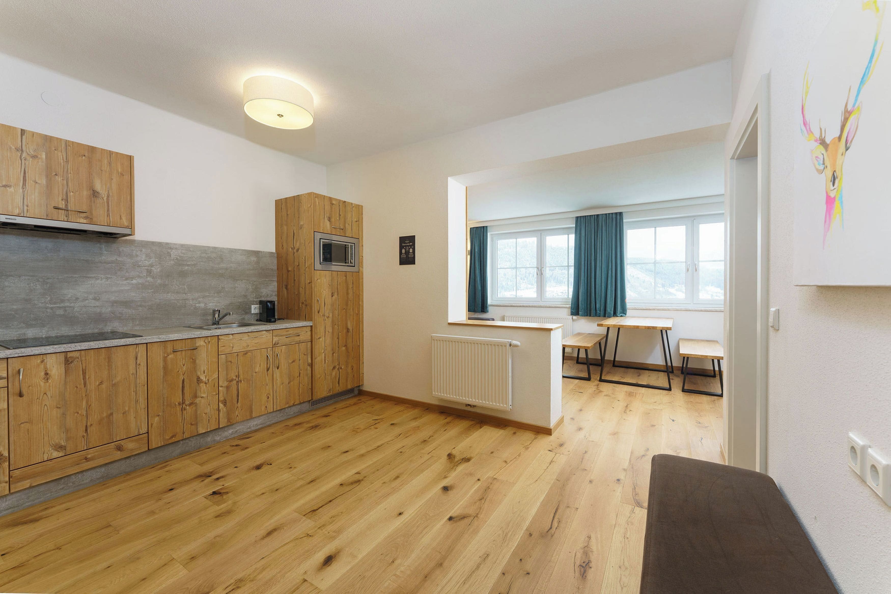 A modern kitchen with wooden cabinets, a built-in microwave, and a large window with curtains.