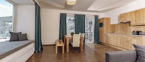 Une cuisine moderne avec des meubles en bois, un coin repas comprenant une table et des chaises, et une grande fenêtre avec des rideaux.