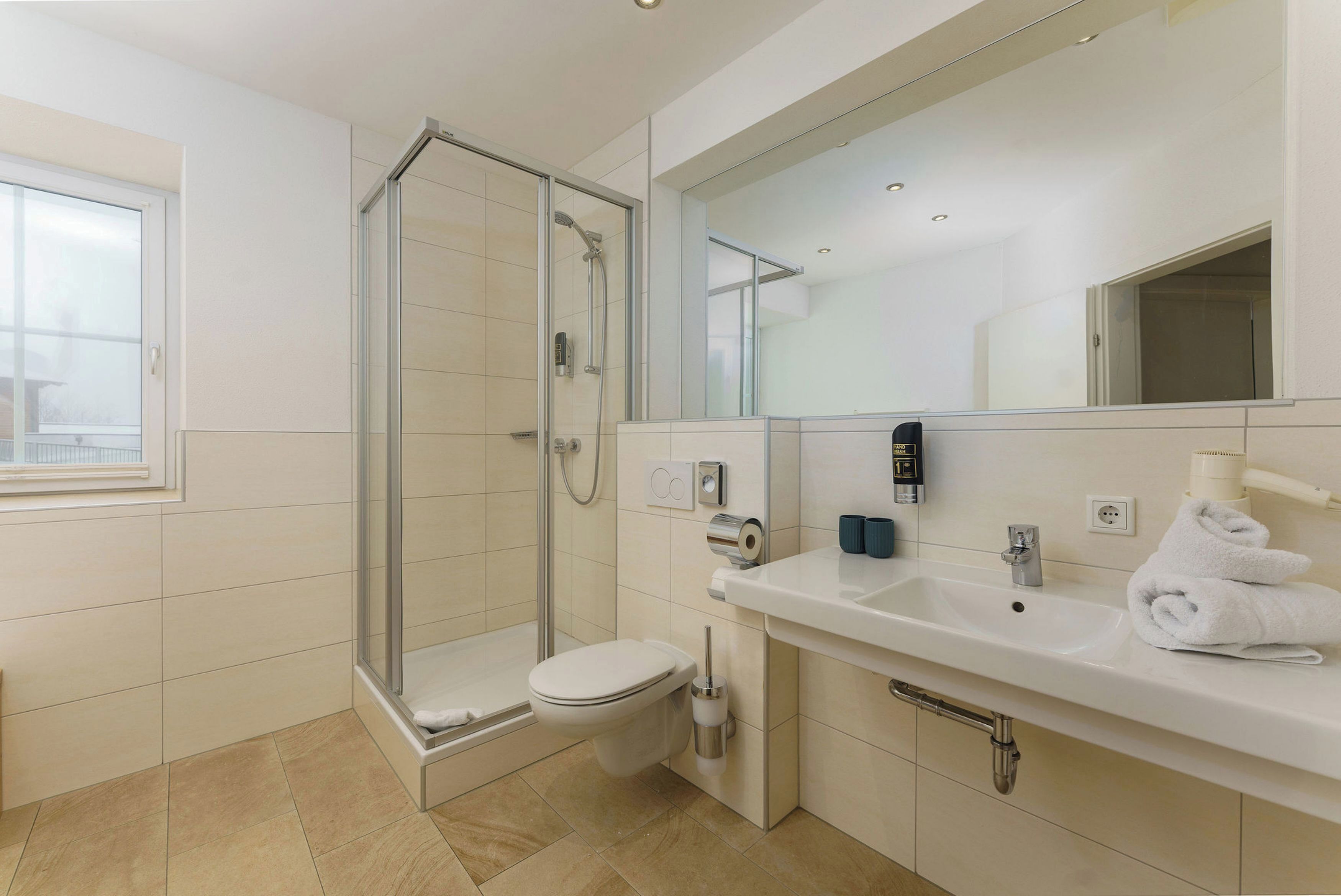 Un baño moderno con ducha de vidrio, inodoro, lavamanos con espejo y ventana.