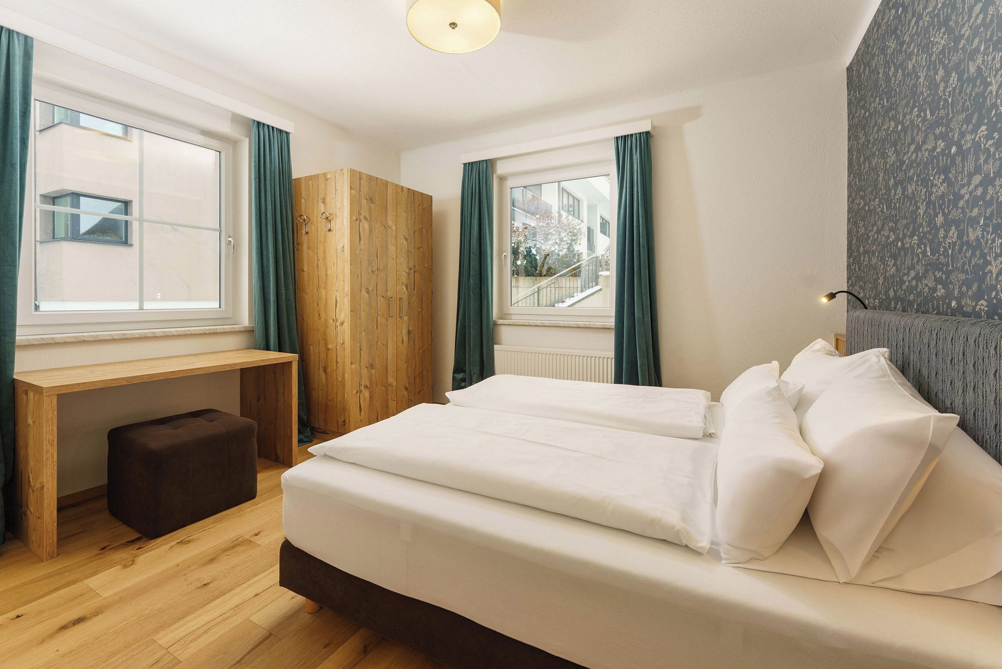 A bedroom with a bed, a wooden desk, and a window.