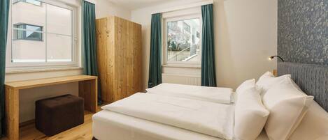 A bedroom with a bed, a wooden desk, and a window.