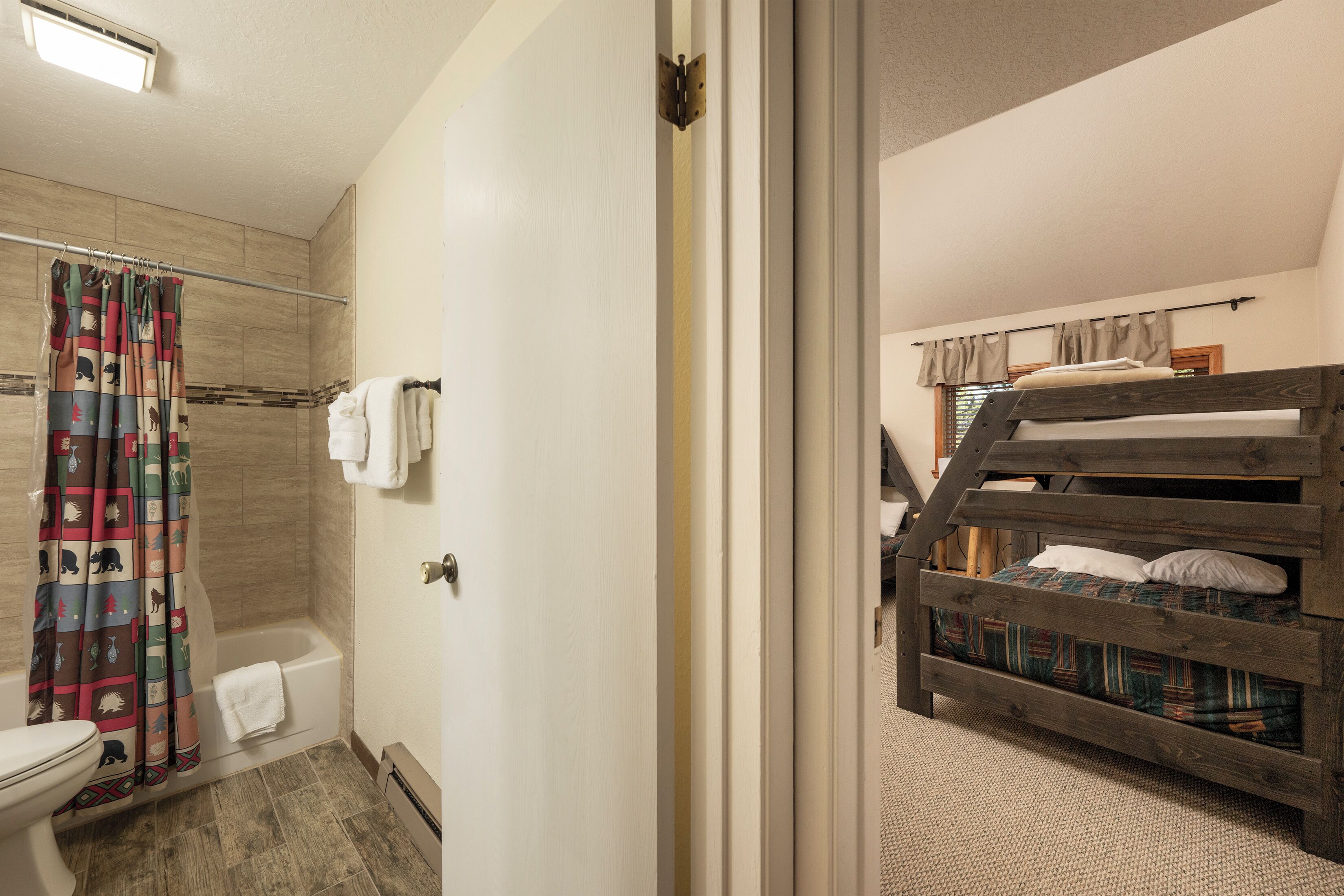 A bathroom with a shower, toilet, and a wooden bunk bed in the adjacent room.