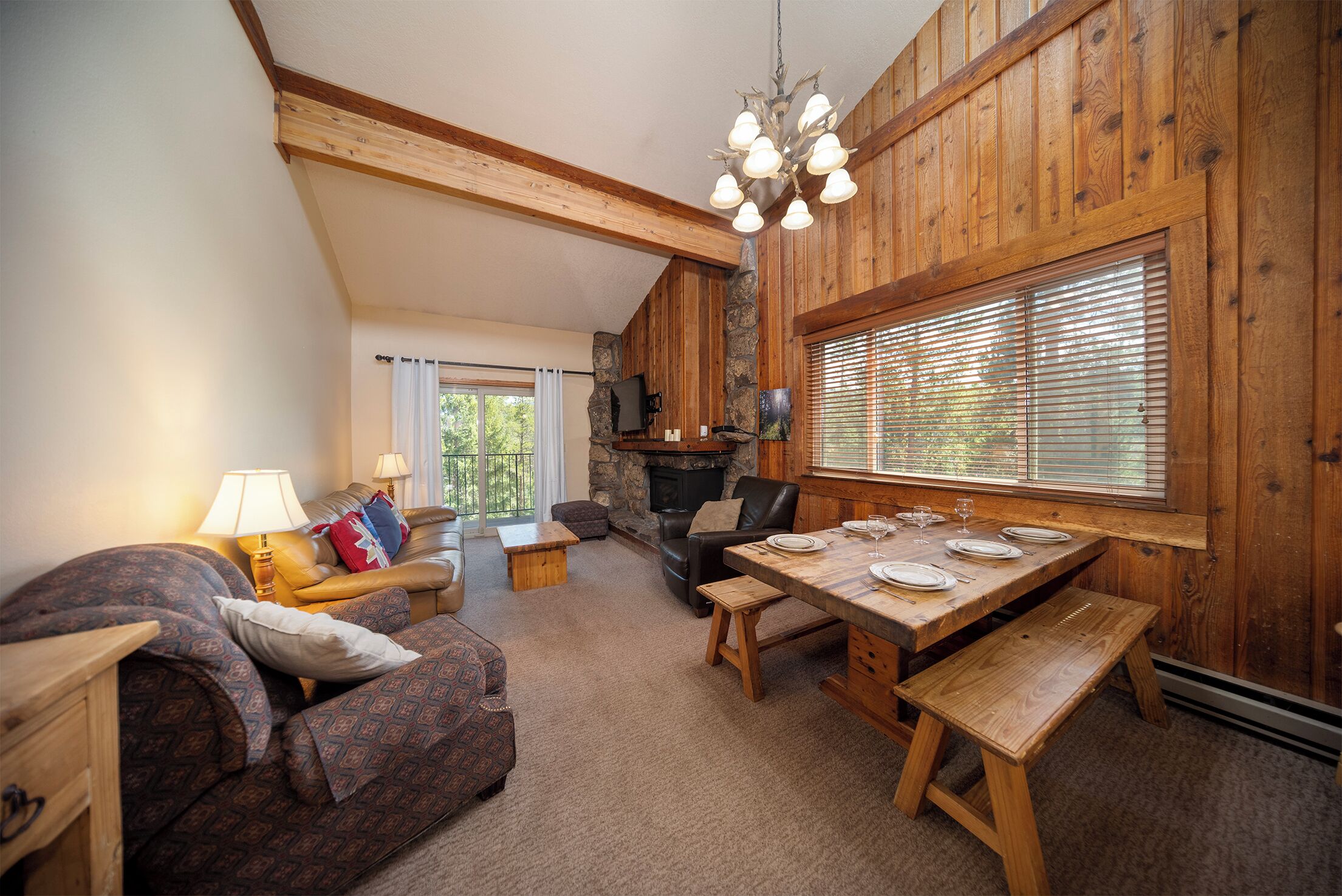 A cozy living room with a fireplace, a dining table set for four, and a comfortable seating area with a sofa and armchairs.