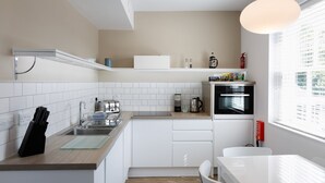 Una cucina moderna con mobili bianchi, forno integrato, macchina da caffè e portaoggetti per coltelli.