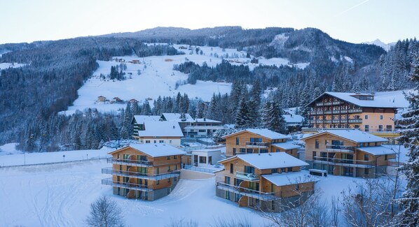 Une station de ski enneigée, avec de nombreux bâtiments en bois, des pistes de ski et un paysage montagneux en toile de fond.