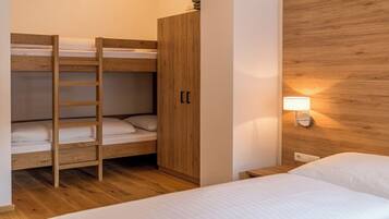 A bunk bed room with a wooden ladder, a wardrobe, and a bedside lamp.