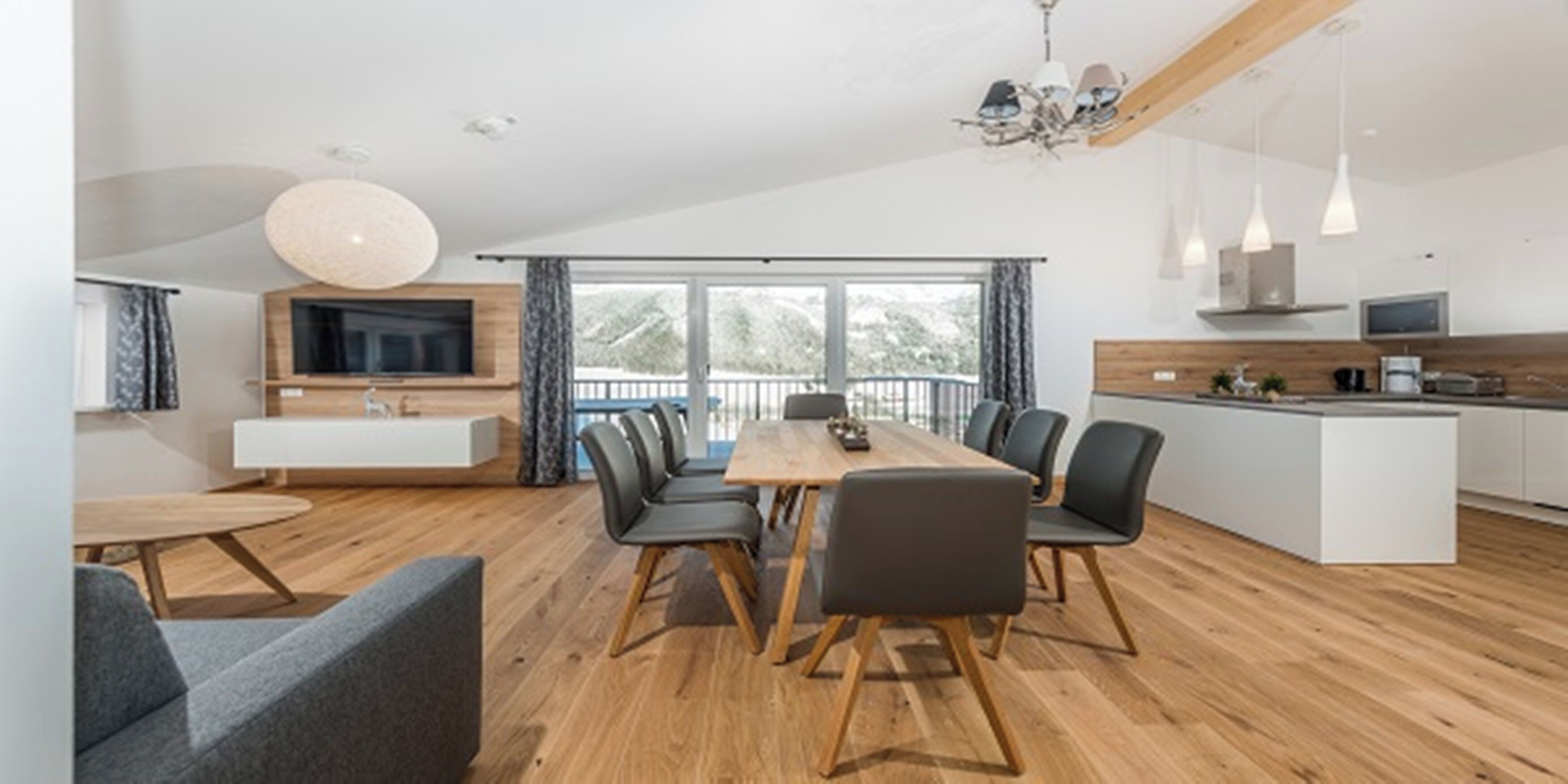 A modern kitchen with a central island, a dining area with a wooden table and chairs, and a large window providing a view of the outdoors.