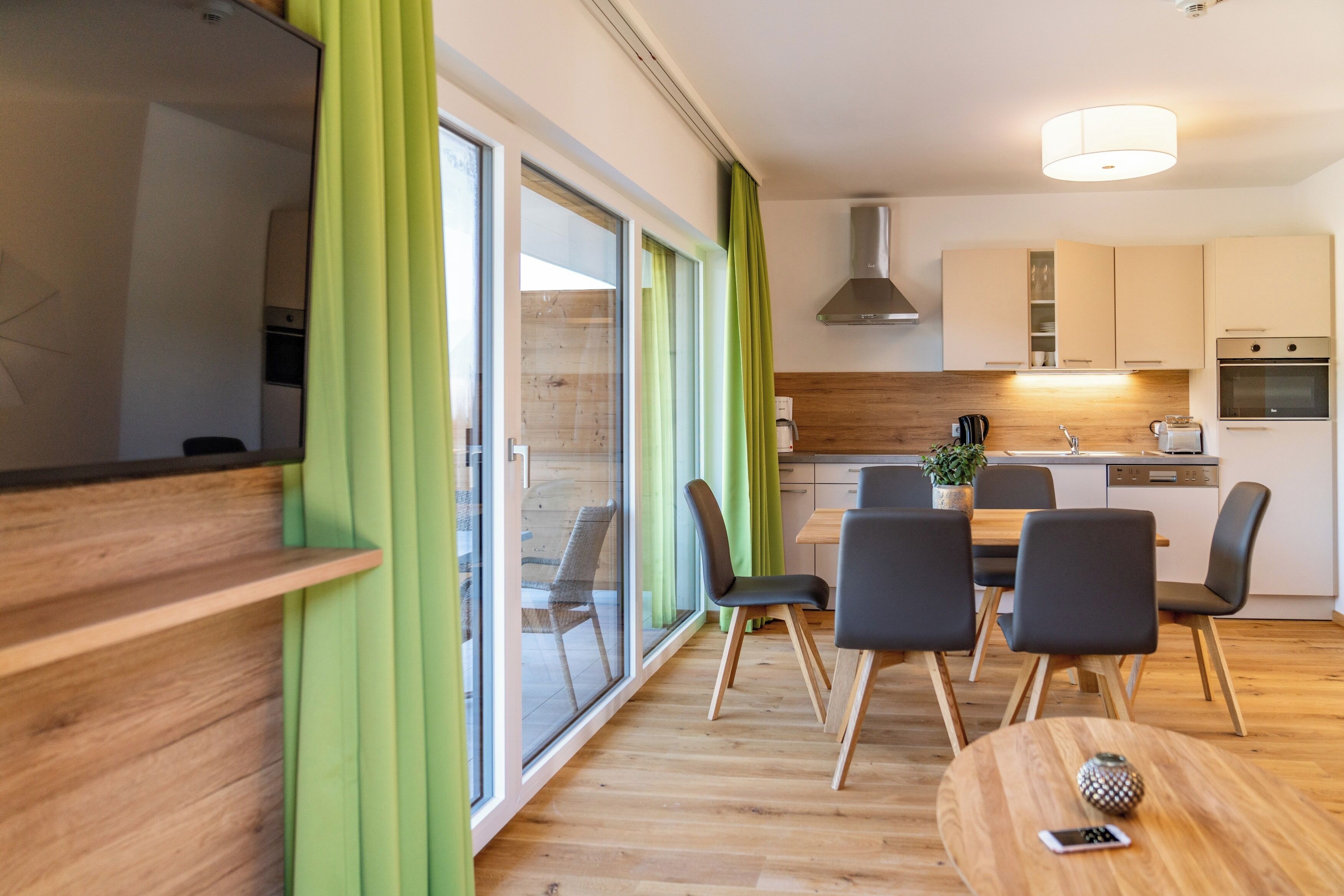 A modern kitchen with wooden cabinets, a built-in oven, and a dining area with a wooden table and chairs.