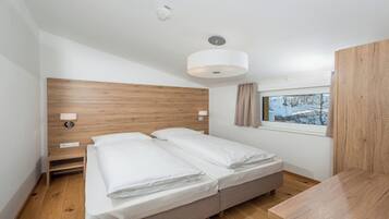 A bedroom with a wooden headboard, two beds, bedside lamps, a window with a view of trees, and a ceiling light.