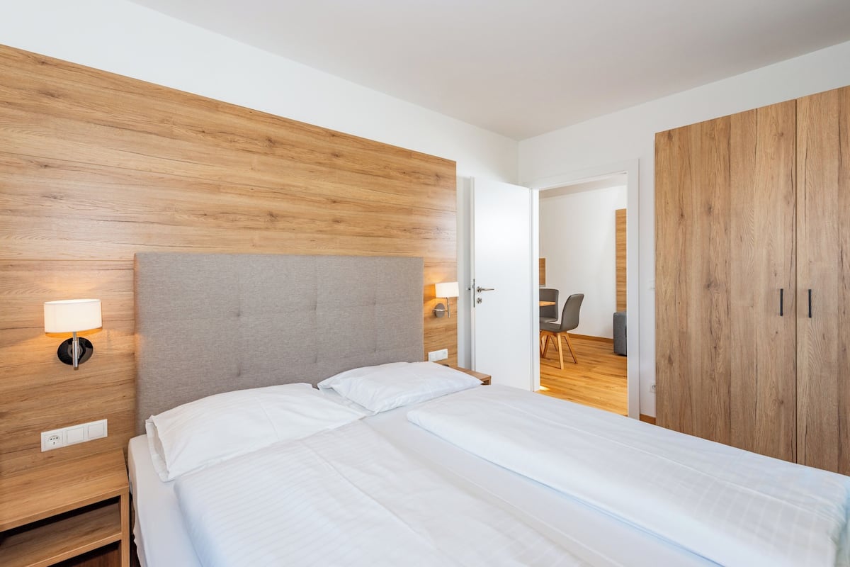 Ett hotellrum med en sänggavel i trä, en säng med vita sängkläder, en sänglampa och en garderob.