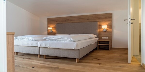A bedroom with a bed, wooden headboard, bedside lamps, and a wooden floor. - Panorama Lodge Premium Apartments (Schladming)