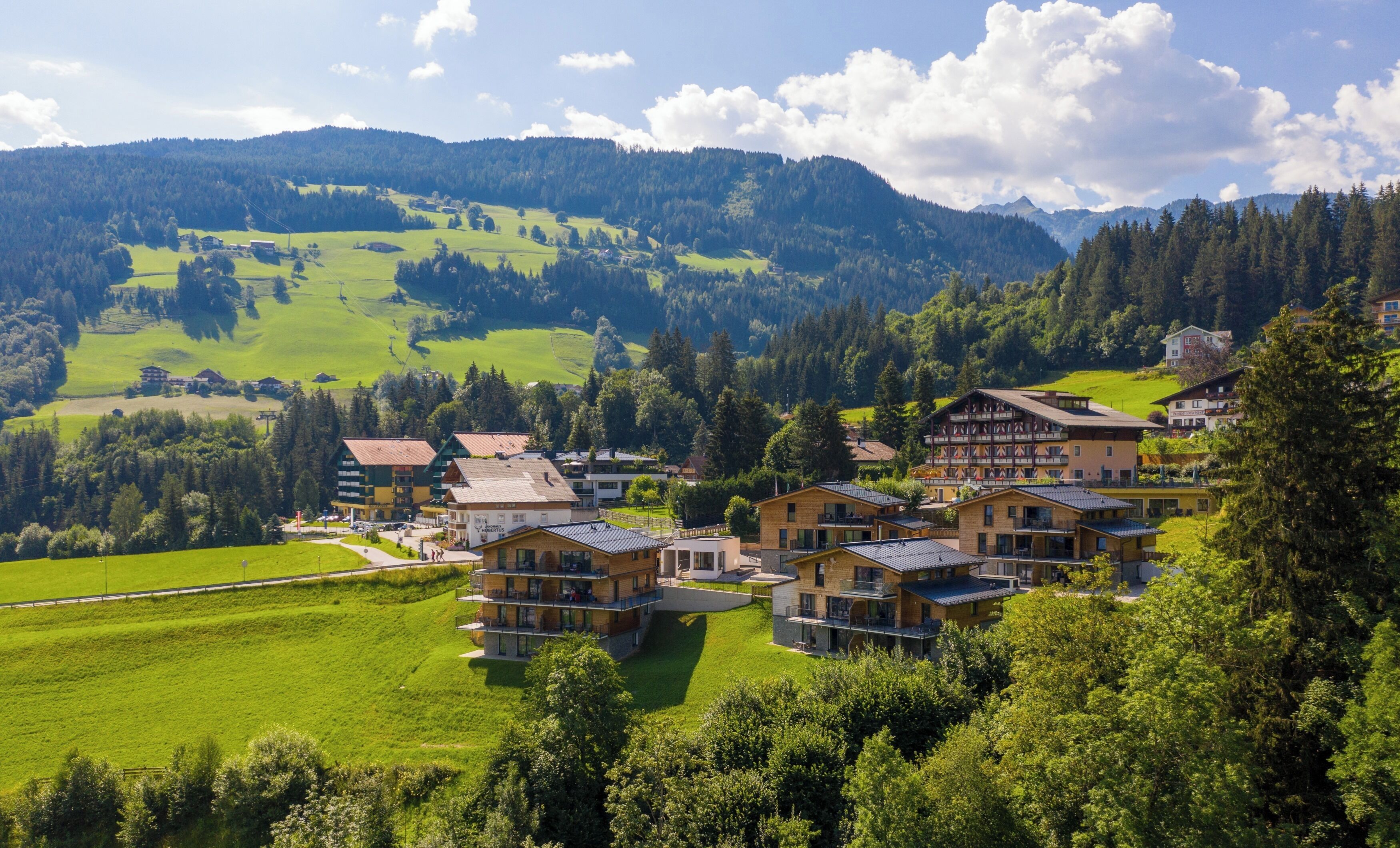 A mountain village with traditional chalet-style buildings, a ski lift, and lush green fields.