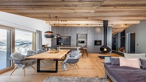 A modern interior with a wooden ceiling, a dining area with a large table and chairs, a sofa, and a fireplace.
