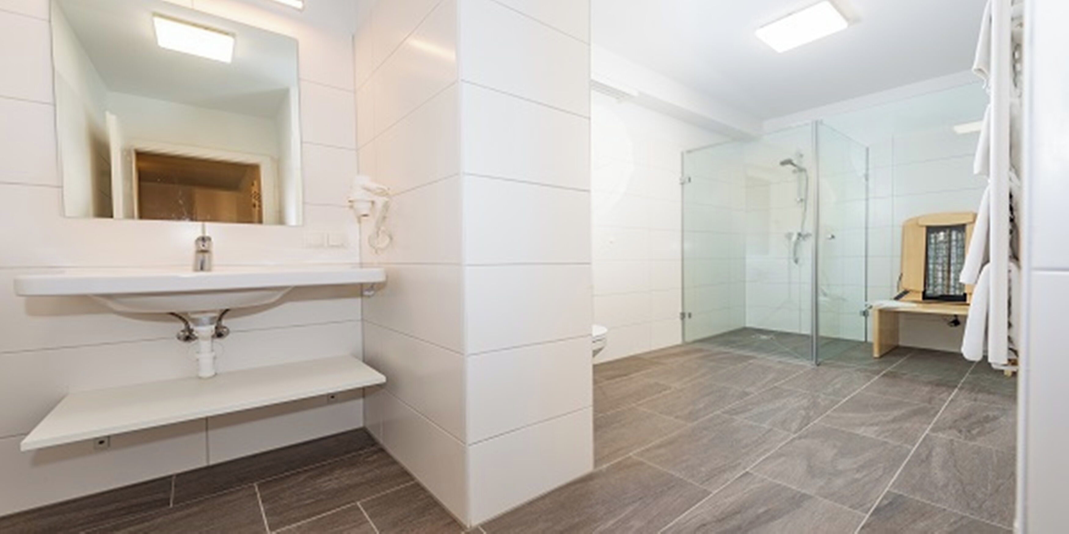 Un baño moderno con lavamanos blanco, espejo y zona de ducha.
