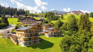 A modern hotel with multiple balconies, a central courtyard, and a view of the surrounding forest and hills.