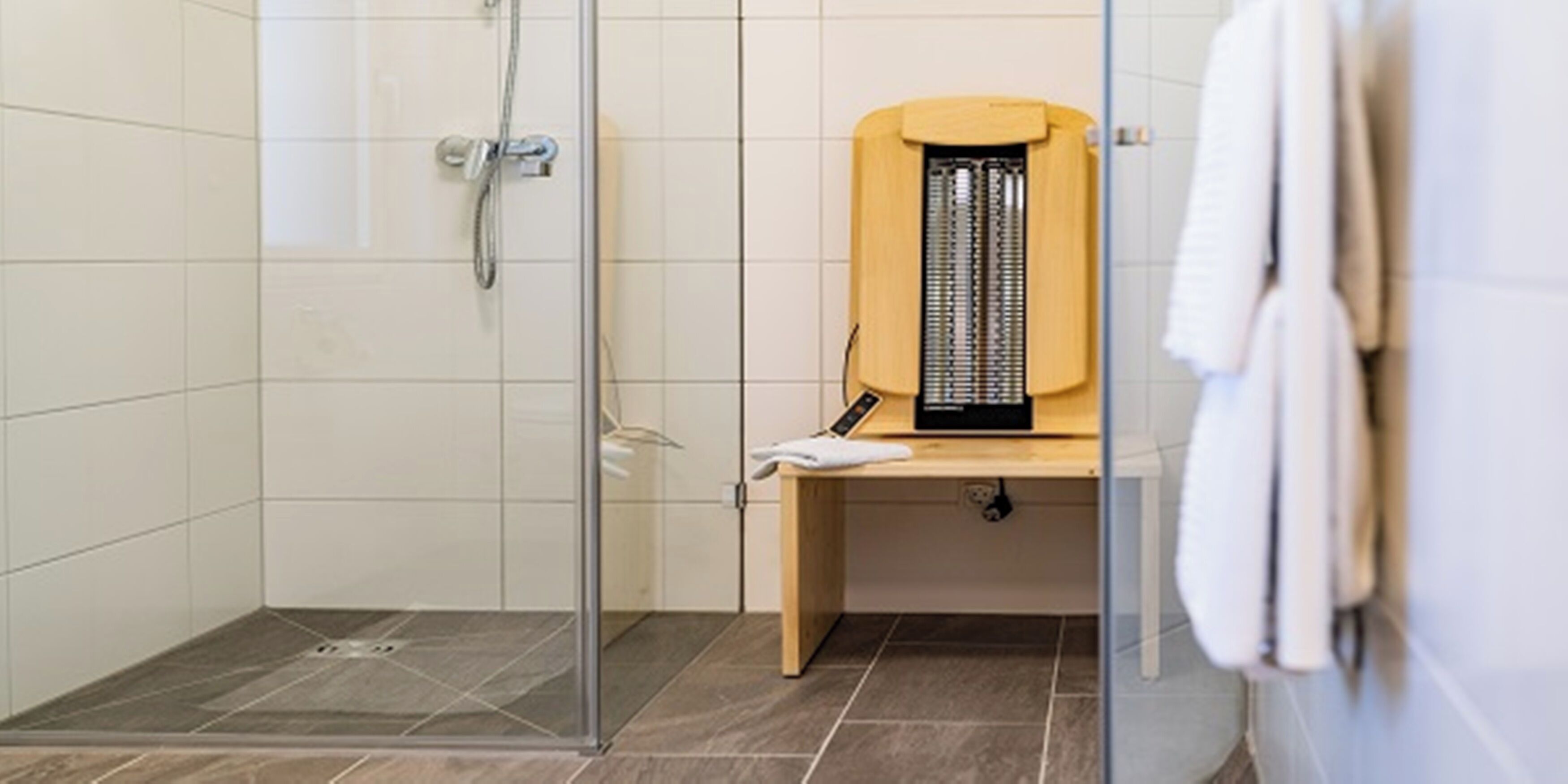 A shower area with a glass door, a wooden bench, and a towel hanging on the wall.