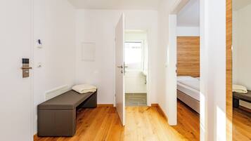 Ein modernes Hotelzimmer mit Holzboden, einem Bett, einer Bank und einer Tür zu einem weiteren Raum.