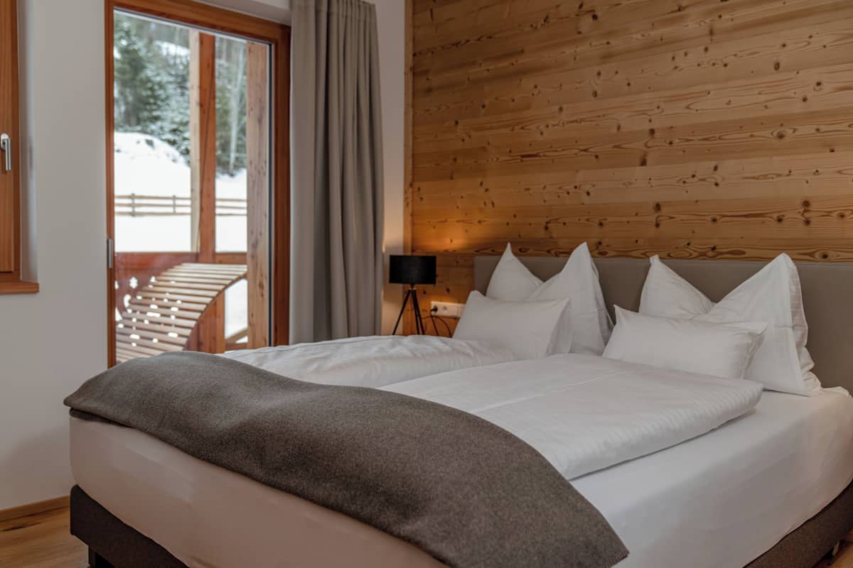 A bedroom with a large bed, wooden walls, a window with curtains, and a view of a snowy landscape.