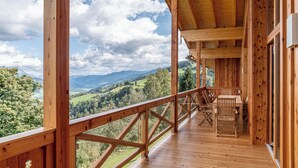Terraza de madera con mesa y sillas, con vistas a un paisaje montañoso.