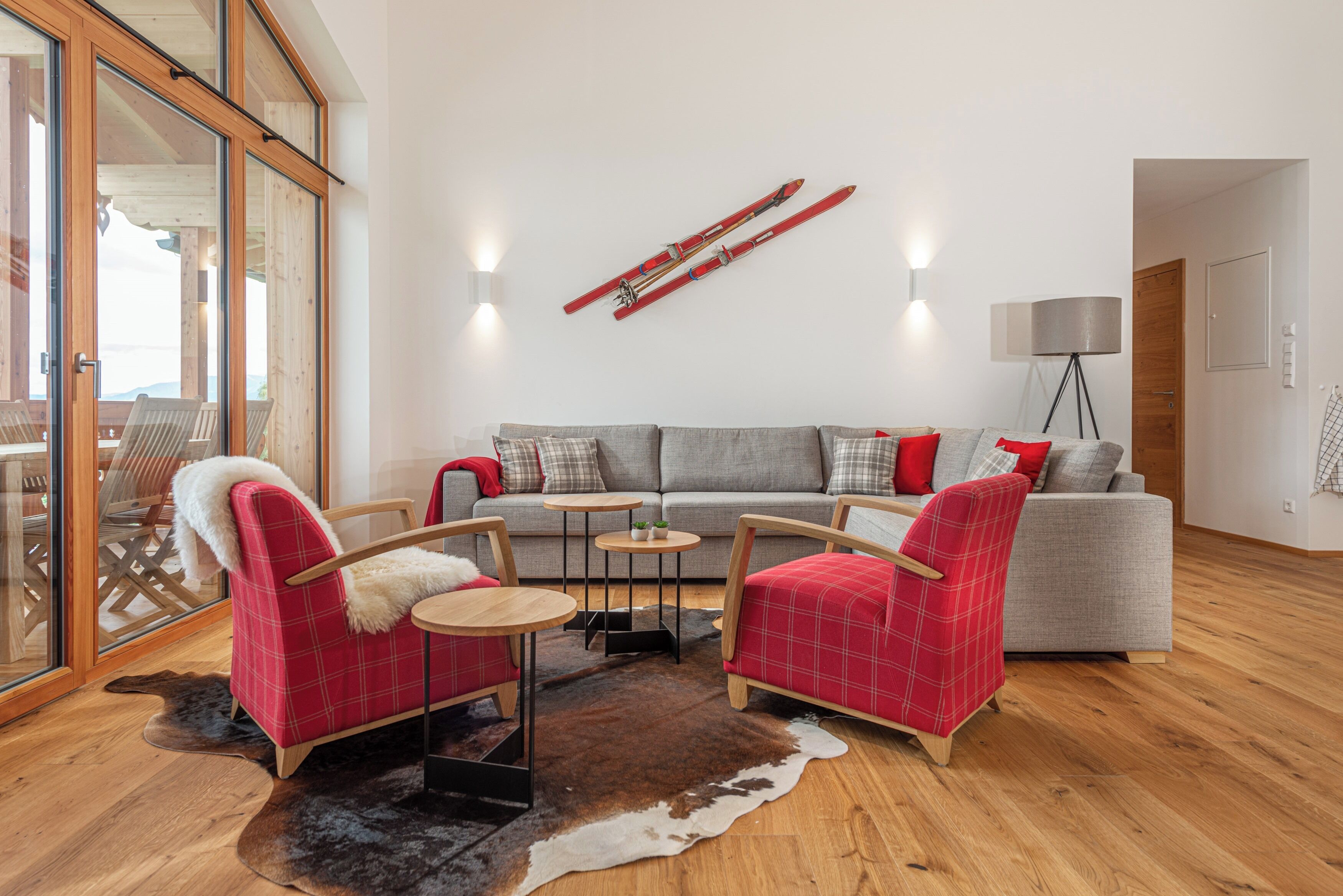 Una sala de estar moderna con un sofá gris, sillones rojos escoceses, un ventanal que da al exterior y un esquí en la pared.